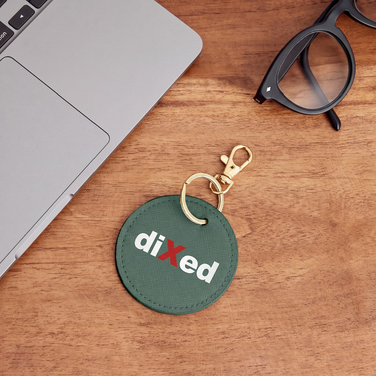 Grüner Schlüsselanhänger mit diXed-Logo neben Laptop und Brille auf einem Holztisch