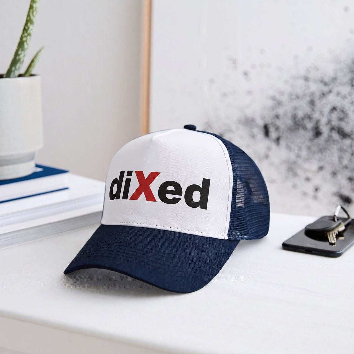 Trucker-Cap in Weiß und Navy mit diXed-Logo auf einem Sideboard